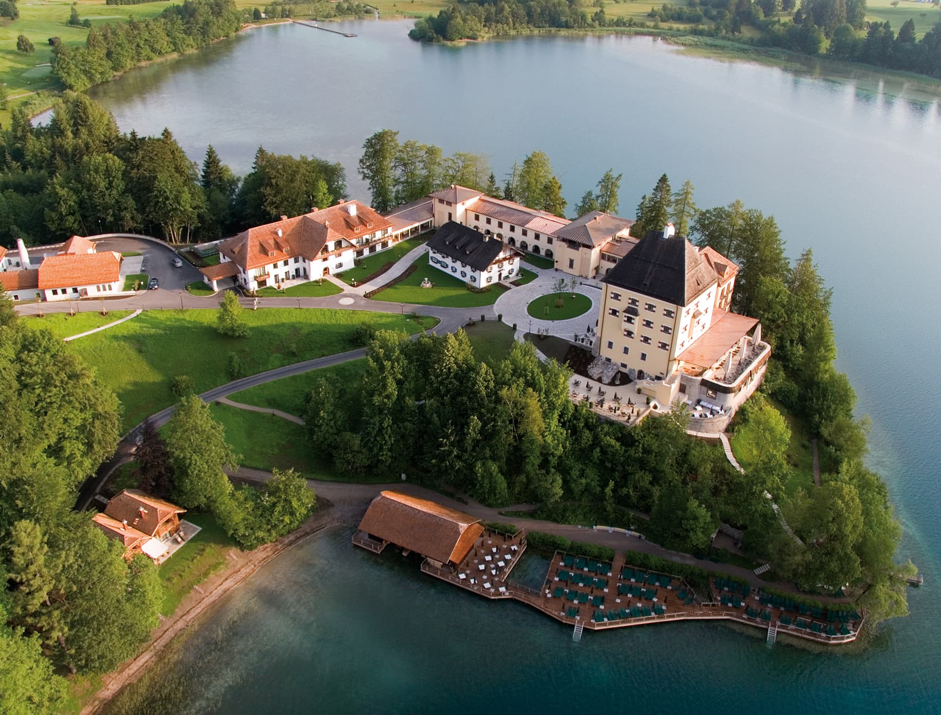 Luftbild eines Schlosses mit Nebengebäuden auf einer Landzunge am See